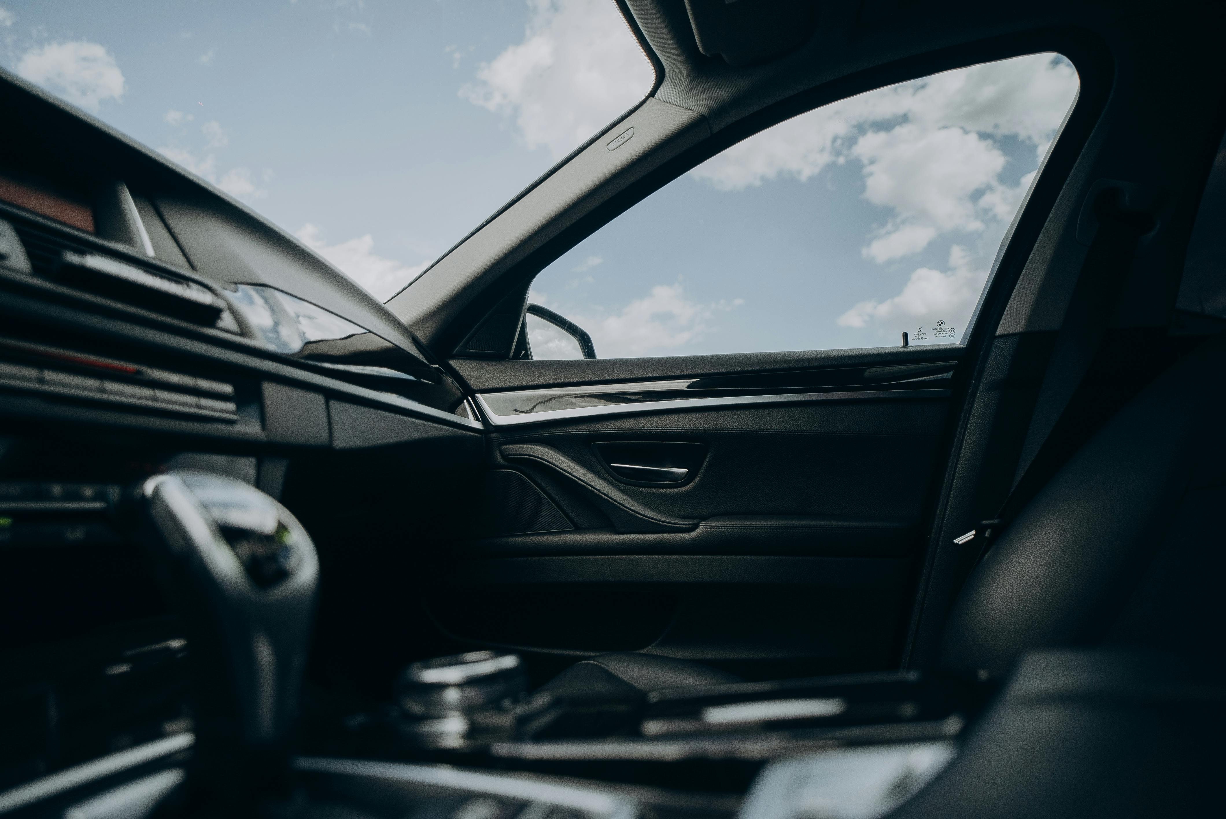 Interior view of a car passenger side door and leather seat with a clear sky visible through the window.